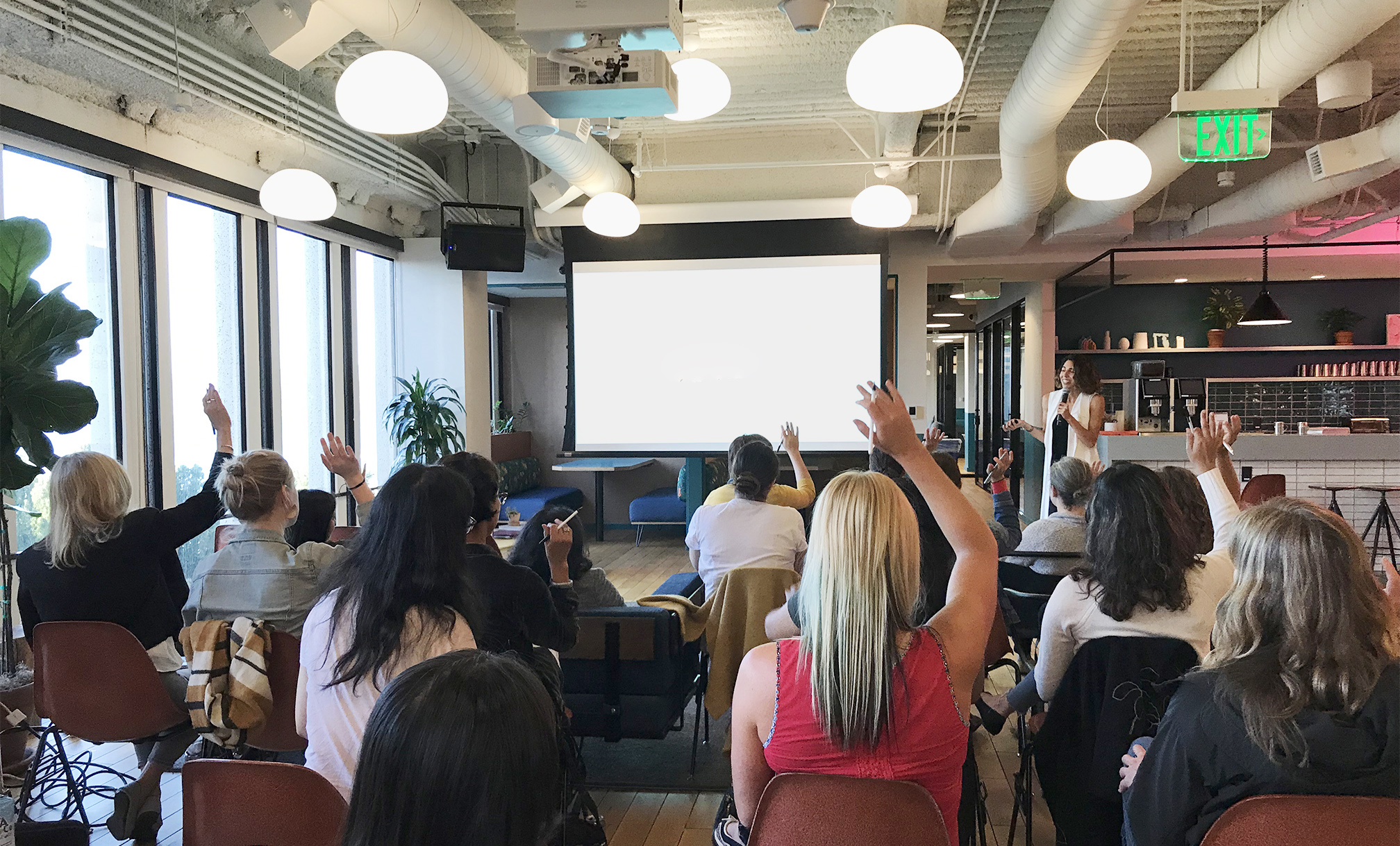 Dalia speaking at the front of a room with the audience raising their hands
